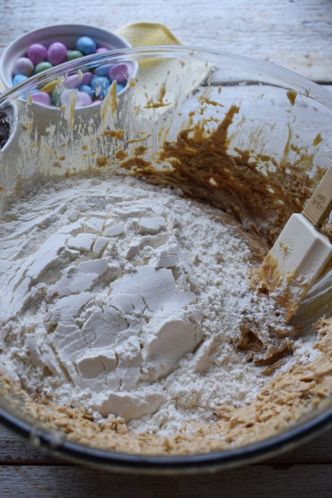 Cookie dough in a glass mixing bowl with flour and candy mix-ins